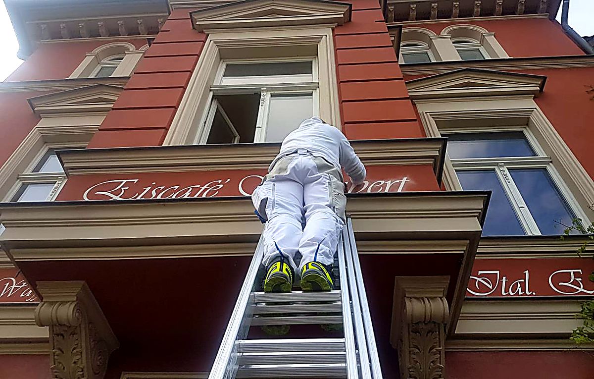 Maler steigt eine Leiter hoch, um ein Fenster zu streichen